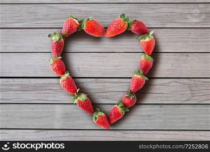 valentines day and romantic concept - heart shaped frame made of fresh strawberries over grey wooden boards background. heart shaped frame made of strawberries