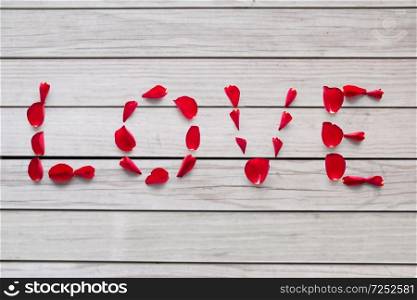 valentines day and romantic concept - word love made of red rose petals over grey wooden boards background. word love made of red rose petals