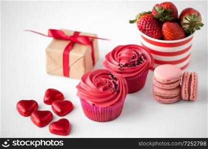valentines day and sweets concept - close up of frosted cupcakes, red heart shaped chocolate candies, macarons, strawberries and gift box. close up of red sweets for valentines day