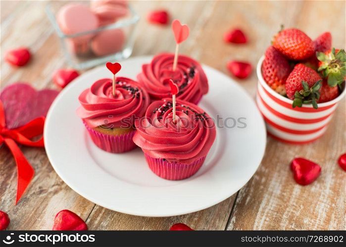 valentines day and sweets concept - close up of frosted cupcakes, red heart shaped chocolate candies, lollipops, macarons and strawberries. close up of red sweets for valentines day