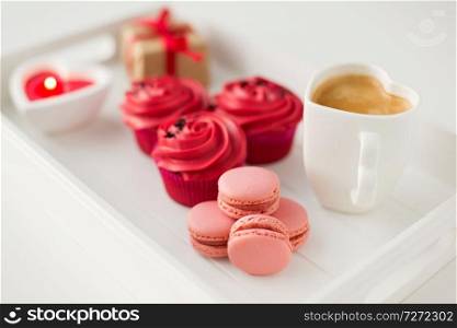 valentines day and sweets concept - close up of pink macarons, cupcakes with red buttercream frosting, heart shaped coffee cup, candle and gift box on tray. close up of red sweets for valentines day