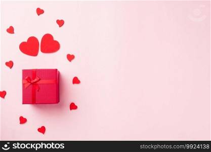 Valentines’ day background. Red gift box with ribbon bow and wood red hearts shaped composition greeting card for love isolated on pink background with copy space. Top View from above