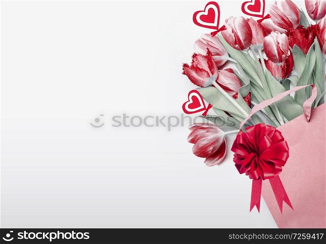 Valentines day background. Red tulips in shopping bag decorated with bow, ribbon and hearts. Holiday shopping concept. Romance floral composing. Flowers bunch. Greeting card or sale coupon.