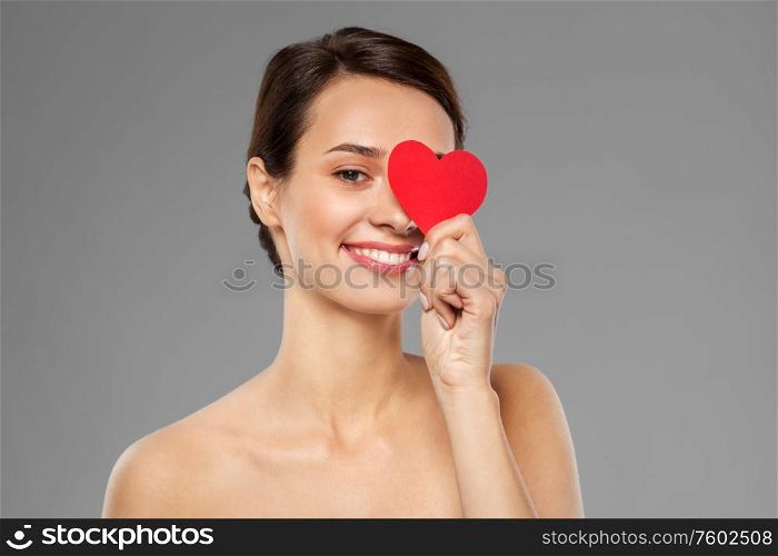 valentines day, beauty and love concept - happy smiling young woman closing one eye with pink heart shape over grey background. beautiful woman closing one eye with pink heart