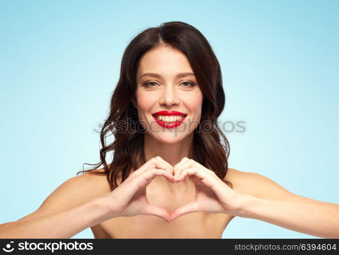 valentines day, beauty and people concept - happy smiling young woman with red lipstick making hand heart gesture over blue background. beautiful woman with red lipstick and hand heart