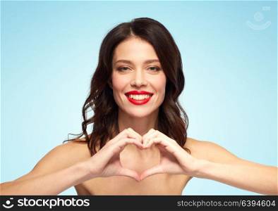 valentines day, beauty and people concept - happy smiling young woman with red lipstick making hand heart gesture over blue background. beautiful woman with red lipstick and hand heart