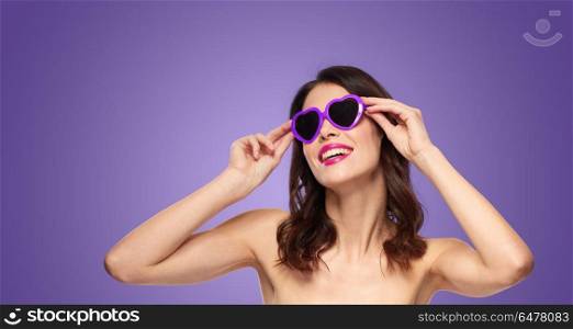 valentines day, beauty and people concept - happy smiling young woman with pink lipstick and heart shaped sunglasses over ultra violet background. woman with pink lipstick and heart shaped shades. woman with pink lipstick and heart shaped shades