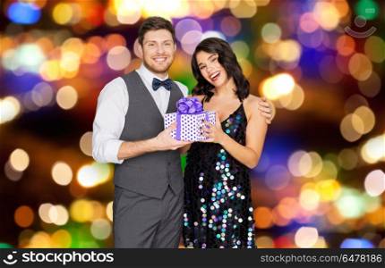 valentines day, birthday and holidays concept - happy couple with gift box at party over festive lights background. happy couple with gift box at birthday party. happy couple with gift box at birthday party