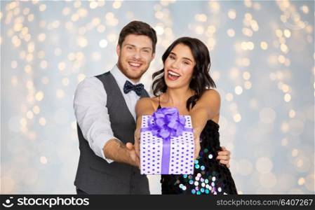 valentines day, birthday, anniversary and holidays concept - happy couple with gift box at party over festive lights background. happy couple with gift box at birthday party