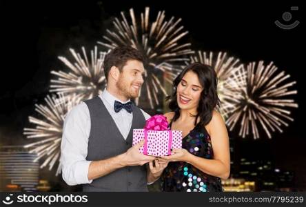 valentines day, birthday, anniversary and holidays concept - happy couple with gift box at party over firework lights at night city background. happy couple with gift box at birthday party