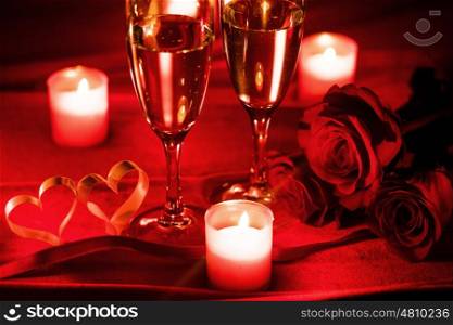 Valentines day celebration, glasses of champagne, candles, roses and hearts on red silk