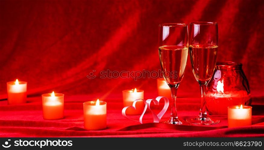 Valentines day celebration, glasses of champagne, candles, roses and hearts on red silk. Champagne and candles