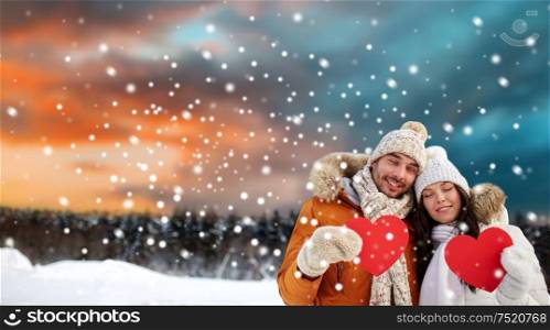 valentines day, christmas and holidays concept - happy couple holding blank red hearts over winter forest background. happy couple with red hearts over winter landscape
