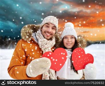 valentines day, christmas and holidays concept - happy couple holding blank red hearts over winter forest background. happy couple with red hearts over winter landscape