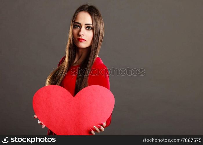 Valentines day concept. Brunette long hair young woman in red dress holding big heart love symbol dark gray background