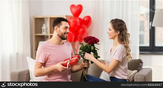 valentines day, couple, relationships and people concept - happy man giving woman flowers and present at home. happy man giving woman flowers and present at home