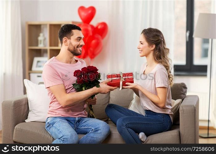valentines day, couple, relationships and people concept - happy man giving woman flowers and present at home. happy man giving woman flowers and present at home