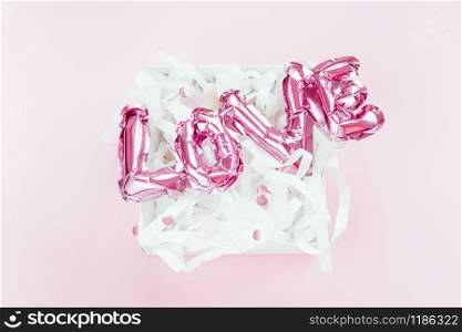 Valentines Day creative concept. Inflatable pink glossy foil balloon word Love in present box pink background. Top view flat lay copy space. Holiday celebration wedding bachelorette party decoration