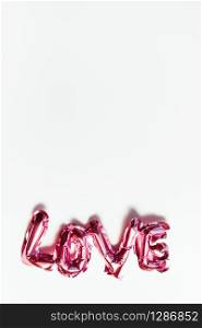Valentines Day creative concept. Inflatable pink glossy foil balloon word sign Love with shadows isolated on white background. Top view flat lay with copy space. Light and bright composition