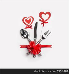 Valentines day dinner table setting with cutlery, red ribbon and hearts on white background, top view