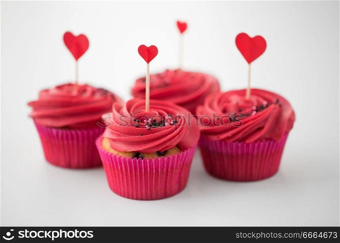 valentines day, food, baking and pastry concept - close up of cupcakes or muffins with red buttercream frosting and heart cocktail sticks on white background. close up of cupcakes with heart cocktail sticks