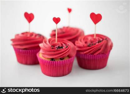 valentines day, food, baking and pastry concept - close up of cupcakes or muffins with red buttercream frosting and heart cocktail sticks on white background. close up of cupcakes with heart cocktail sticks