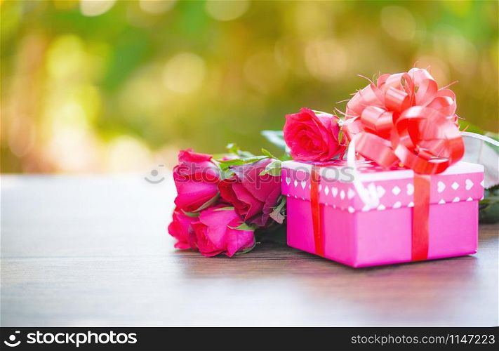 Valentines day gift box flower love concept / Pink gift box with ribbon bow red roses flower on wooden table nature green background