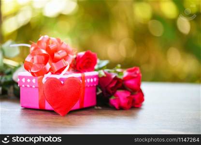 Valentines day gift box flower love concept / Pink gift box with ribbon bow red roses flower and heart on wooden table nature green background