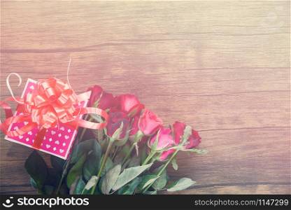 Valentines day gift box flower love concept / pink gift box with ribbon bow red roses flower on wooden table rustic background tone vintage top view copy space