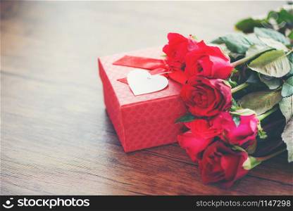 Valentines day gift box flower love concept / Red gift box with ribbon bow red roses flower on wooden table rustic background tone vintage