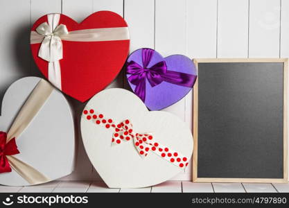 Valentines Day gift boxes. Heart shaped Valentines Day gift boxes and blackboard on white wooden background