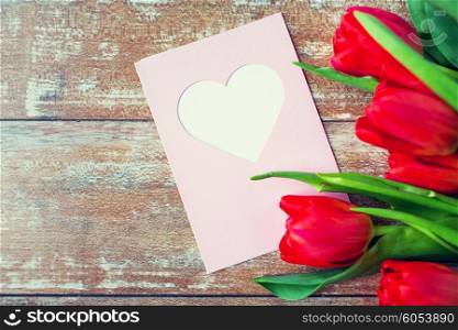valentines day, greeting, love and holidays concept - close up of red tulips and greeting card with heart