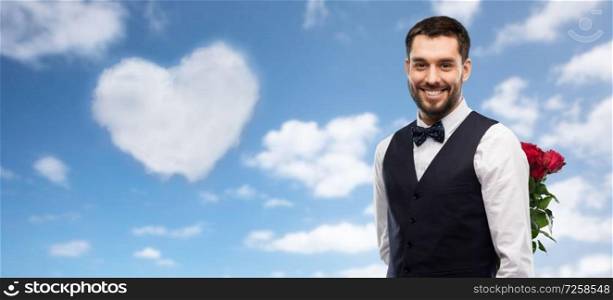 valentines day, greeting people concept - happy man in party clothes with red roses behind his back over blue sky and heart shaped cloud background. happy man with red roses behind his back