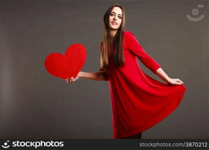 Valentines day happiness and relationships concept. Brunette woman long hair girl in red dress holding heart love symbol dancing pose dark gray background