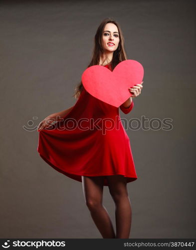 Valentines day happiness and relationships concept. Brunette woman long hair girl in red dress holding heart love symbol dancing pose dark gray background