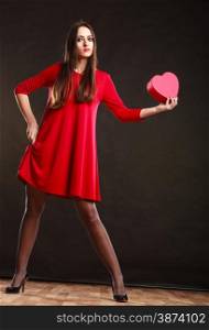 Valentines day happiness and relationships concept. Brunette woman long hair girl in red dress holding heart love symbol dancing pose on dark gray background.