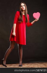 Valentines day happiness and relationships concept. Brunette woman long hair girl in red dress holding heart shaped gift box love symbol dark gray background.