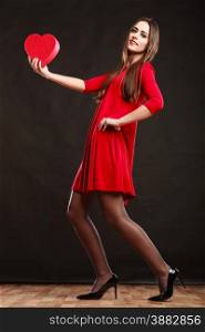 Valentines day happiness and relationships concept. Brunette woman long hair girl in red dress holding heart love symbol dancing pose on dark gray background.