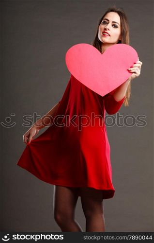 Valentines day happiness and relationships concept. Brunette woman long hair girl in red dress holding heart love symbol dancing pose dark gray background