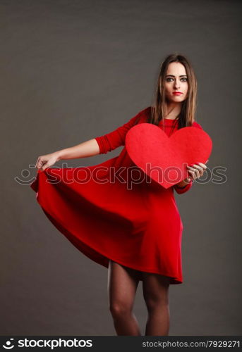 Valentines day happiness and relationships concept. Brunette woman long hair girl in red dress holding heart love symbol dancing pose dark gray background