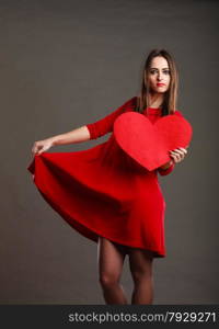 Valentines day happiness and relationships concept. Brunette woman long hair girl in red dress holding heart love symbol dancing pose dark gray background