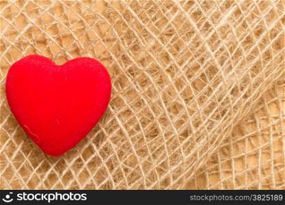 Valentines day, health care or charity concept. Red big heart love symbol on rustic brown bagging cloth background with copy space.