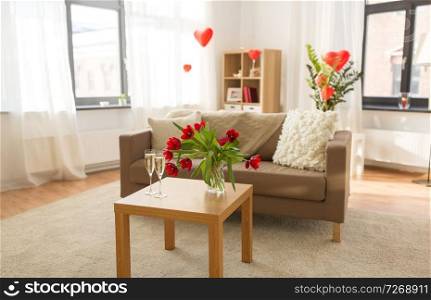 valentines day, holidays and interior concept - two glasses of ch&agne and red flowers on table in living room or home decorated with heart shaped balloons. living room or home decorated for valentines day