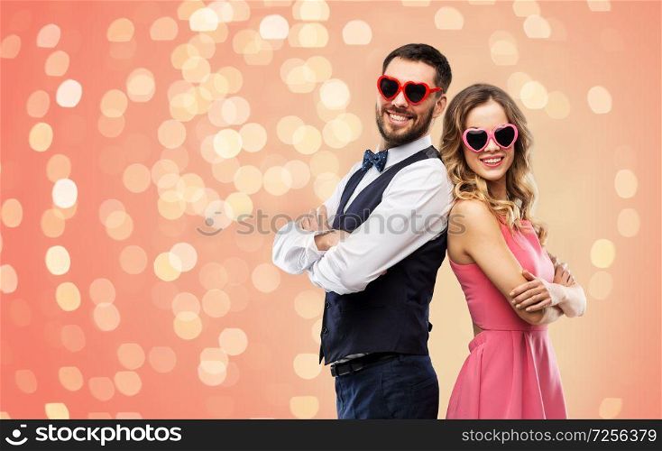 valentines day, love and people concept - happy couple in heart-shaped sunglasses over living coral background and festive lights. happy couple in heart-shaped sunglasses
