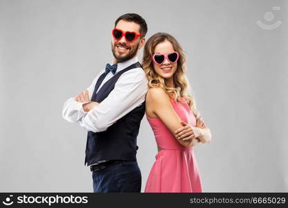 valentines day, love and people concept - happy couple in heart-shaped sunglasses over grey background. happy couple in heart-shaped sunglasses