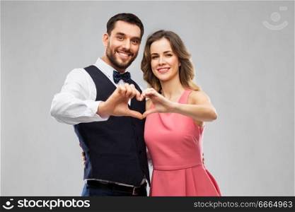 valentines day, love and people concept - happy couple in party clothes making hand heart gesture over grey background. happy couple making hand heart on valentines day