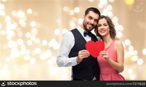 valentines day, love and people concept - happy couple in party clothes with red heart over festive lights background. happy couple with red heart on valentines day