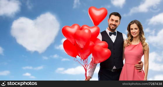 valentines day, love and people concept - happy couple with red heart shaped balloons over blue sky and cloud in shape of heart background. happy couple with red heart shaped balloons