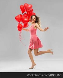 valentines day, love and people concept - happy young woman with red heart shaped balloons over grey background. happy young woman with red heart shaped balloons