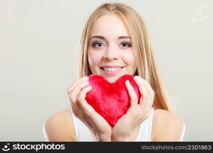 Valentines day love and relationships concept. Blonde long hair young woman holding red heart love symbol studio shot on gray